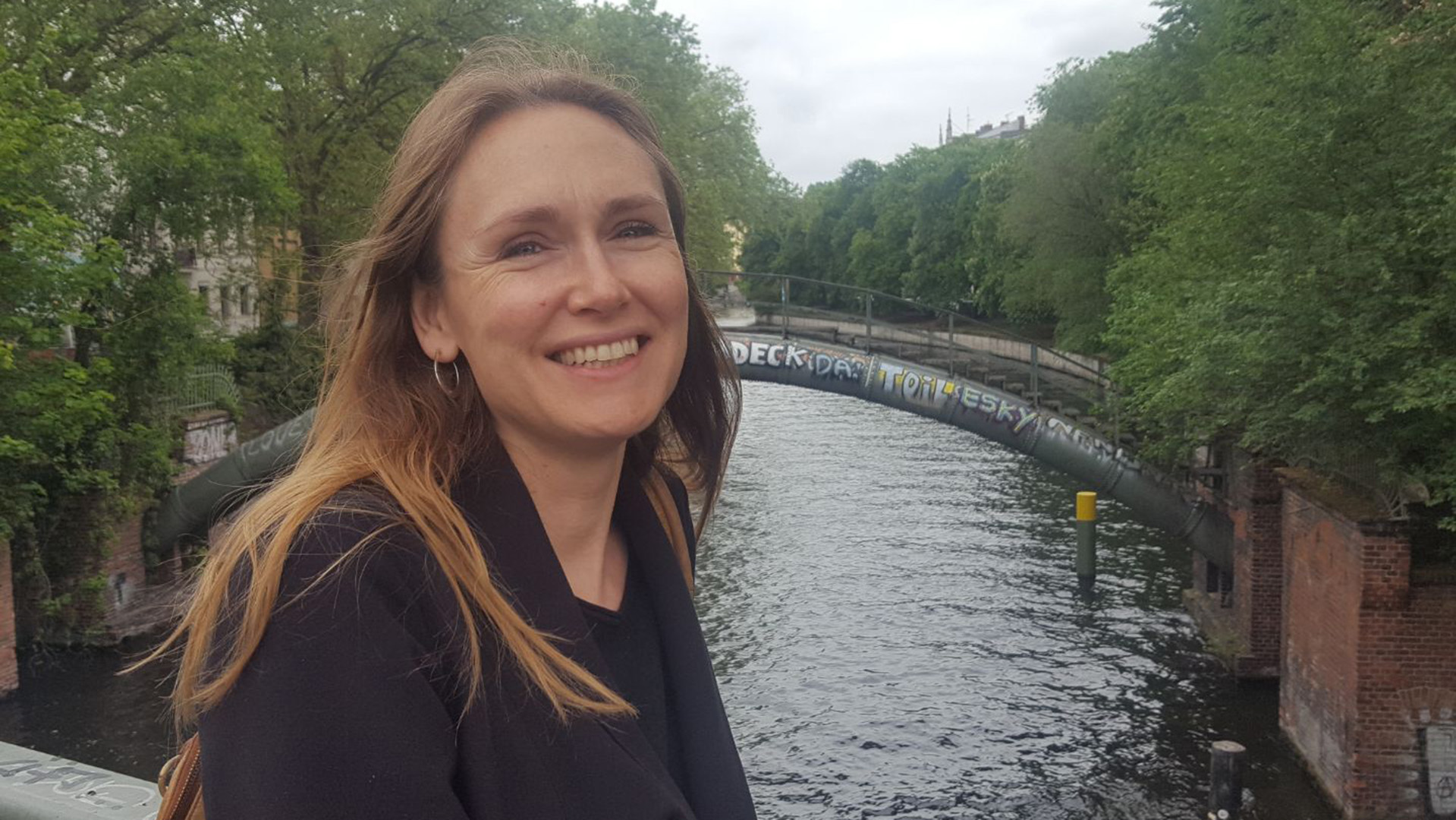 Linnéa Martinsson är gissningsvis i yngre medelåldern. Hon har ljusbrunt långt rakt hår är klädd i en svart kavaj och svart tröja och bär ringar i öronen. Hon står på en bro över ett vattendrag, i bakgrunden finns ytterligare en välvd gångbro. Runt om vattendraget finns gröna träd. Himlen är mulen och Linnéa ler mot fotografen. 