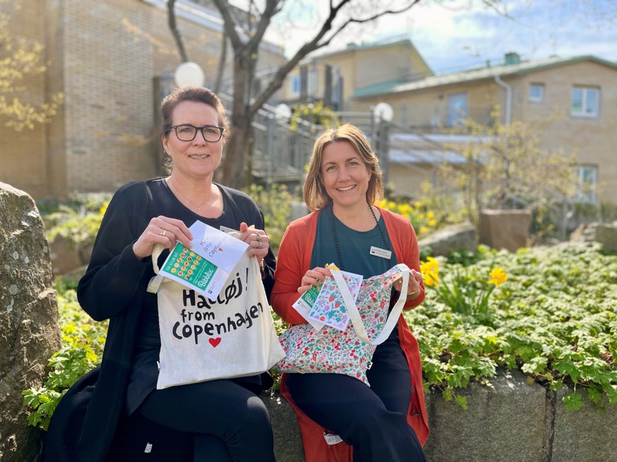 Lotta och Ulrika lutar mot stenmur med varsin tygpåse i famneni