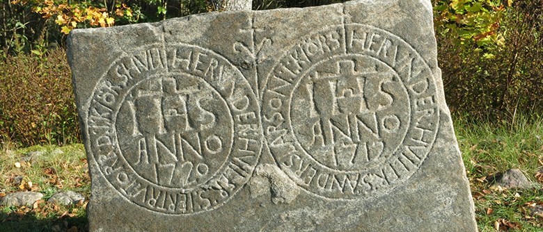 Fotot visar en ålderdomlig gravsten. På stenen kan urskiljas text, bland annat årtalen 1720 samt 1712.