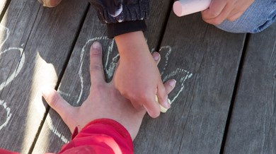 Två barnhänder. Den ena handen ritar av konturerna på den andra handen med en krita.