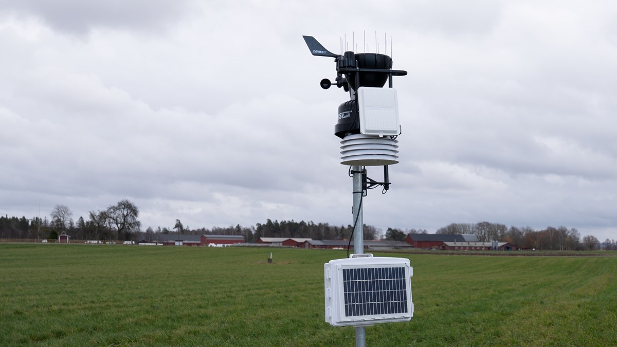 En väderstation av sammankopplade sensorer står på ett fält. I bakgrunden syns Naturbruksskolan Uddetorp.
