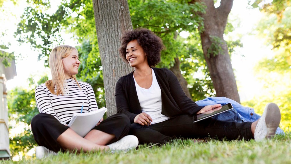 Två flickor som ler mot varandra sittandes på en gräsmatta