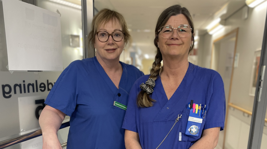 två kvinnliga sjuksköterskor i blå kläder står i en dörröppning.