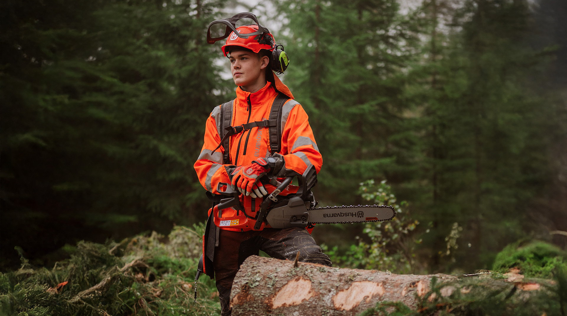 A student wearing protective clothing and a helmet is holding a chainsaw