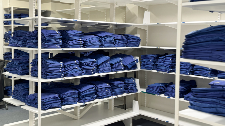 Blåa personalkläder ihopvikta och nytvättade i ett förråd.