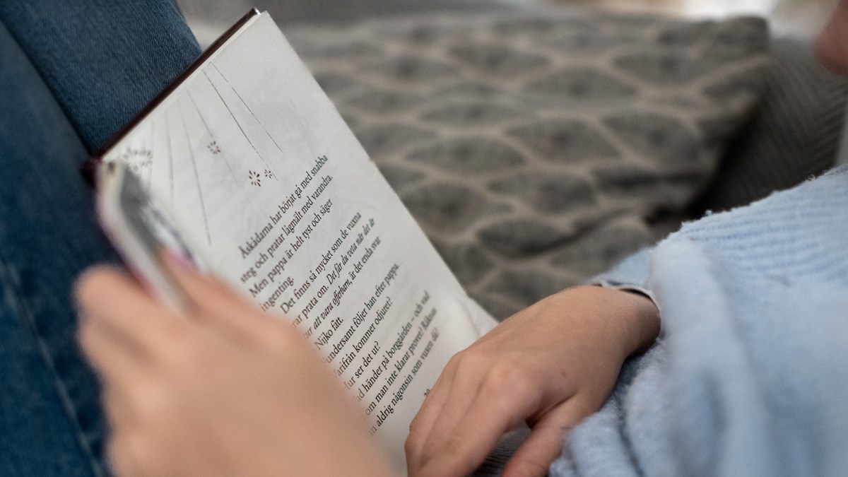 Närbild på ett barn som har en bok i knät som hon läser.