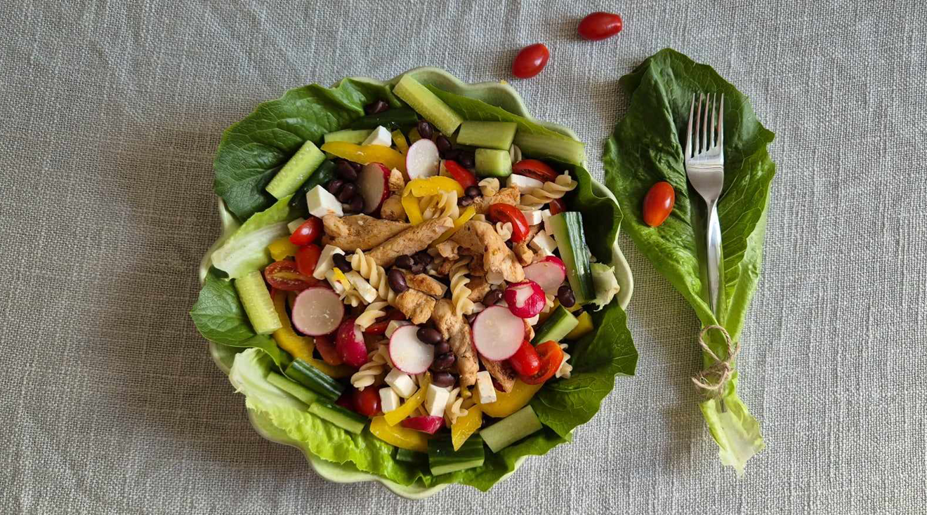 En färgglad pastasallad med kyckling i en skål med gröna blad