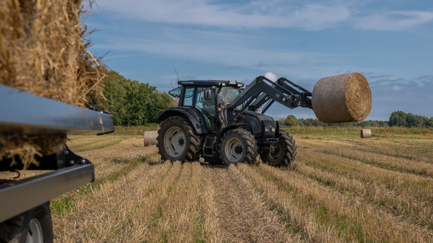 Traktor lyfter halmbal på skördat fält
