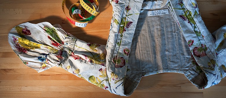 Ett mycket vackert klänningsliv ligger på ett bord.Klänningen är vit med ett färgglatt blommönster. Intill klänningen syns ett måttband.