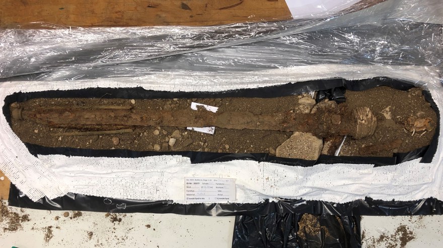 Rester av ett svärd omgivet av jord. Jorden är inlindad i gips och plastfolie.