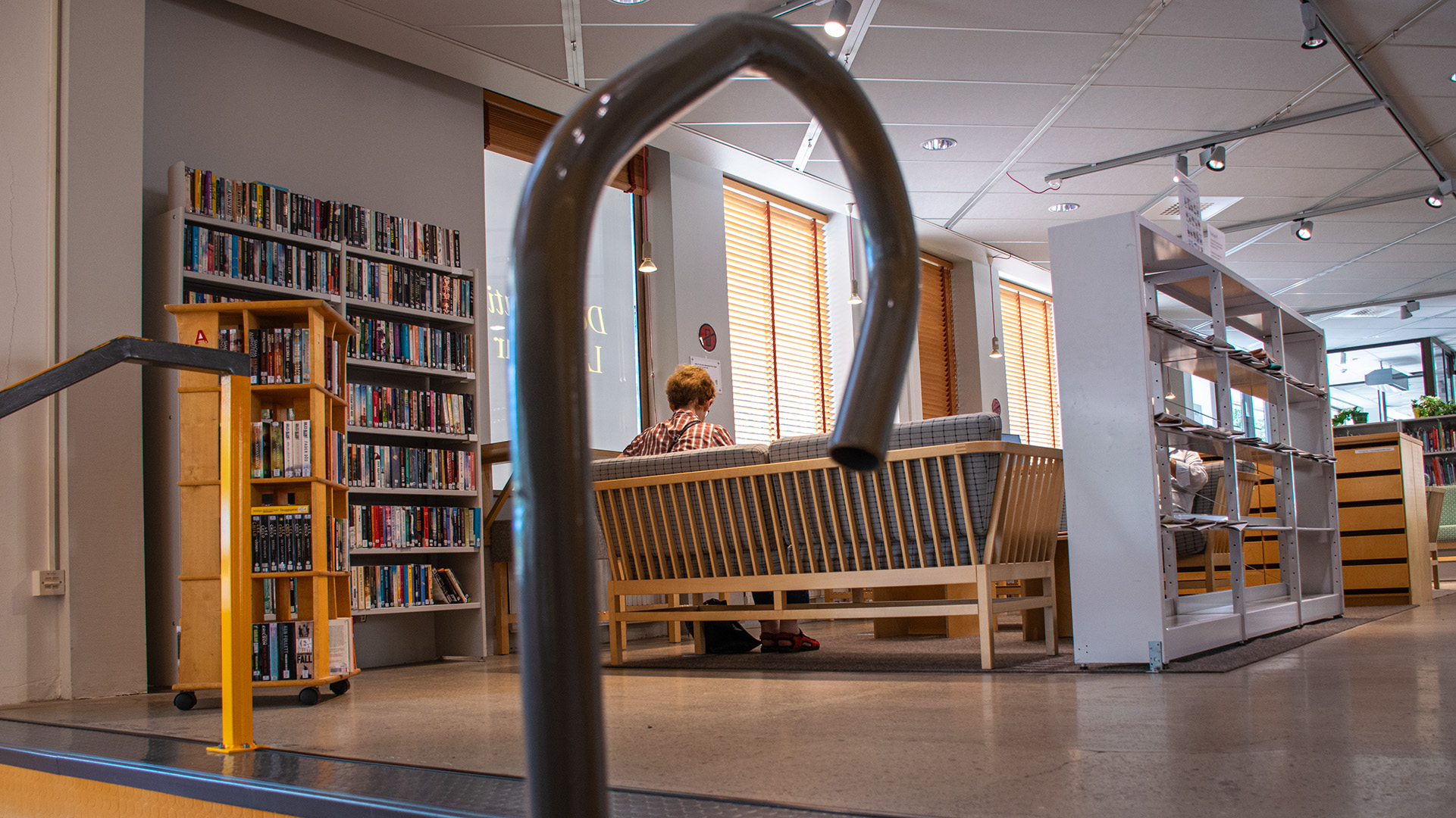 Första våningen på biblioteket i Alingsås. Två soffor står mitt emot varandra, det sitter en person i varje, de är försjunkna i tidningsläsande. 