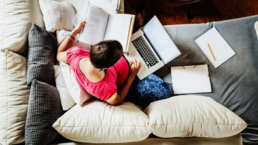 Distansarbete, kvinna sitter i sin hörnsoffa med laptop och dokument i knät