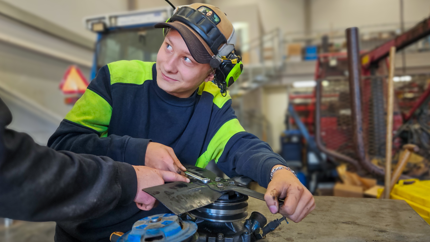 Elev mekar på arbetsbänk med traktor i bakgrunden