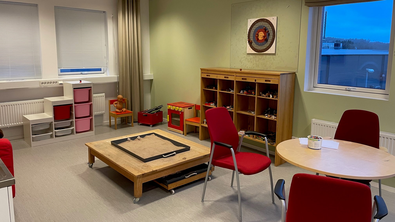 Rum med låga bord och hyllor, leksaksspis och leksaker i backar.