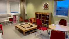 Rum med låga bord och hyllor, leksaksspis och leksaker i backar.