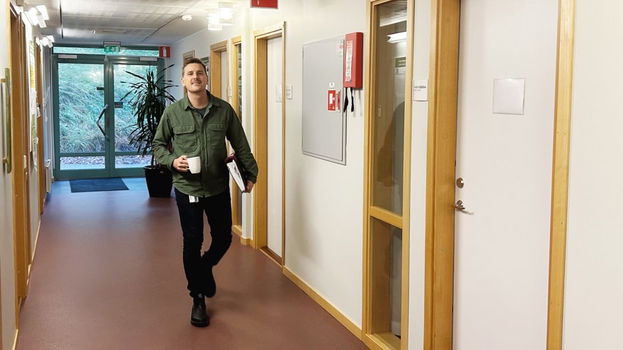 Man går mot kameran i korridor, med kaffekopp i handen