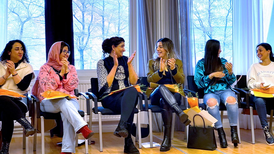 6 deltagare sitter på rad och applåderar och ler