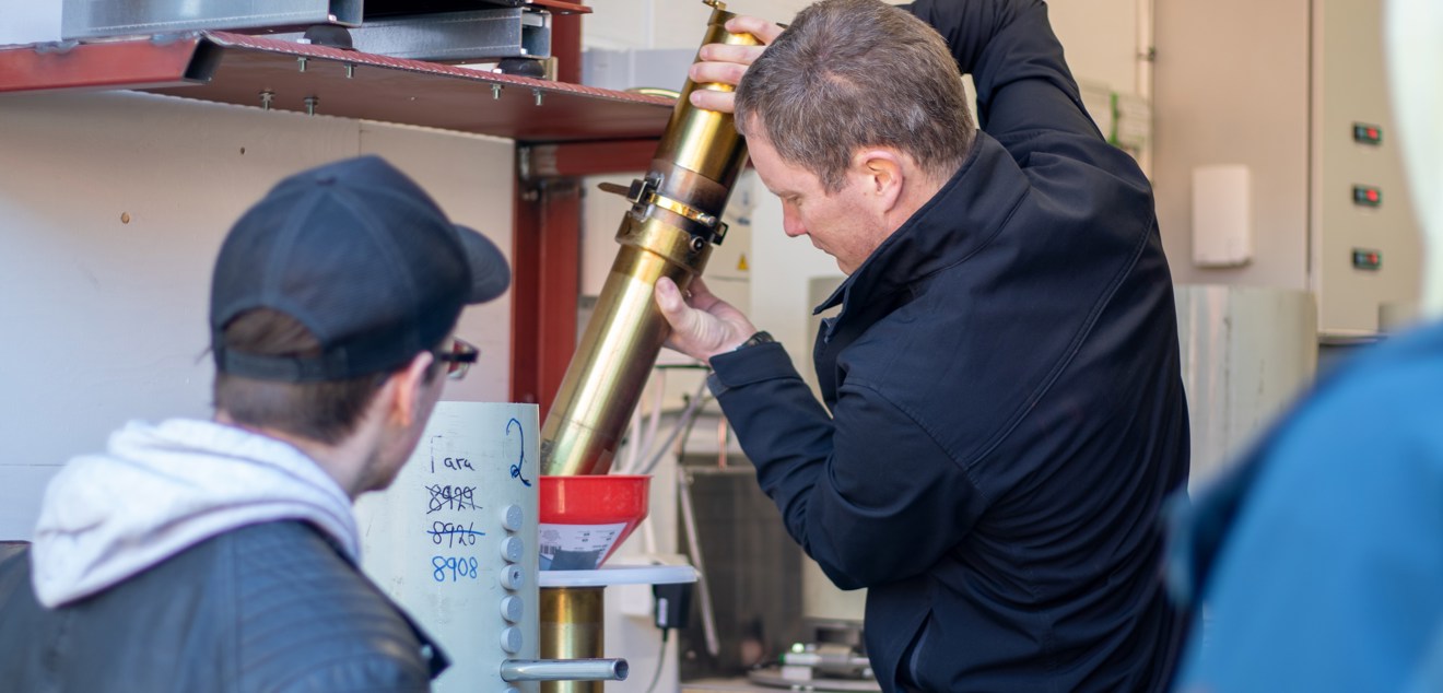 Två elever tittar på när en man häller spannmål ur ett metallrör i en tratt
