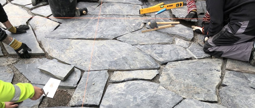 Händer jobbar med stensättning på mark