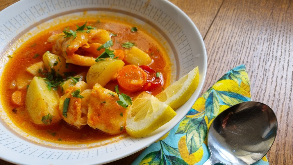 En orangefärgad fisksoppa i en vit skål med citronskivor