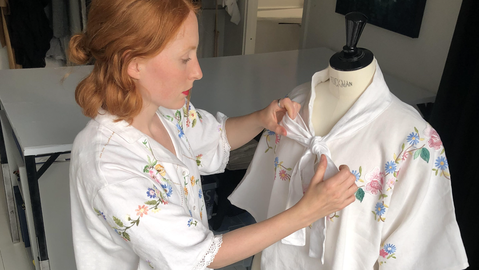 En kvinna med vit skjorta med broderade blommor och spets rättar till en blus på en provdocka