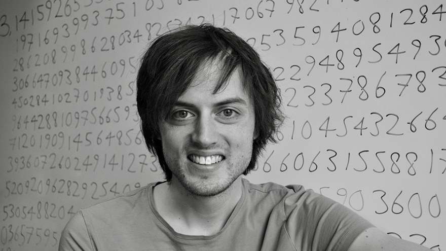 Jonas von Essen har brunt hår med snedlugg. Han är klädd i en t-shirt och står framför en whiteboard som är fylld med skrivna siffror.