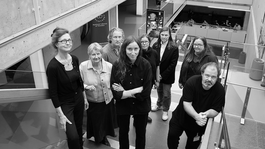 Ett svartvitt foto av åtta personer som står i en trappa. Samtliga tittar upp på fotografen.