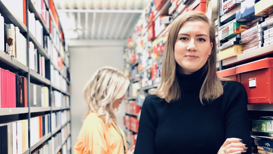 Daria Stroucken-Gerke.står i ett arkiv, bakom henne finns hyllor fyllda med olika typer av material. Hon är i 30-35-årsåldern, har axellångt blont hår och bär en svart polotröja.