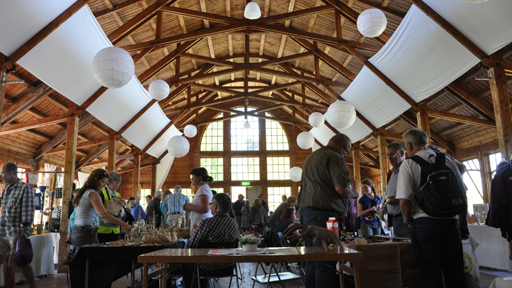 Stort rum i trä med vita tygstycken i taket. Ett myller av människor tittar på slöjdade föremål