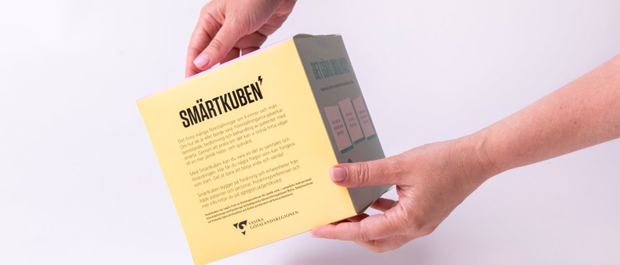Händer håller pappkuben Smärtkuben med text på alla sidor