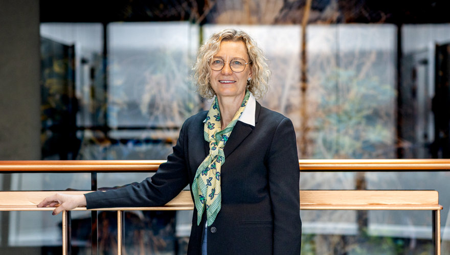 Kvinna i mörk kavaj och gulgrön scarf samt glasögon.