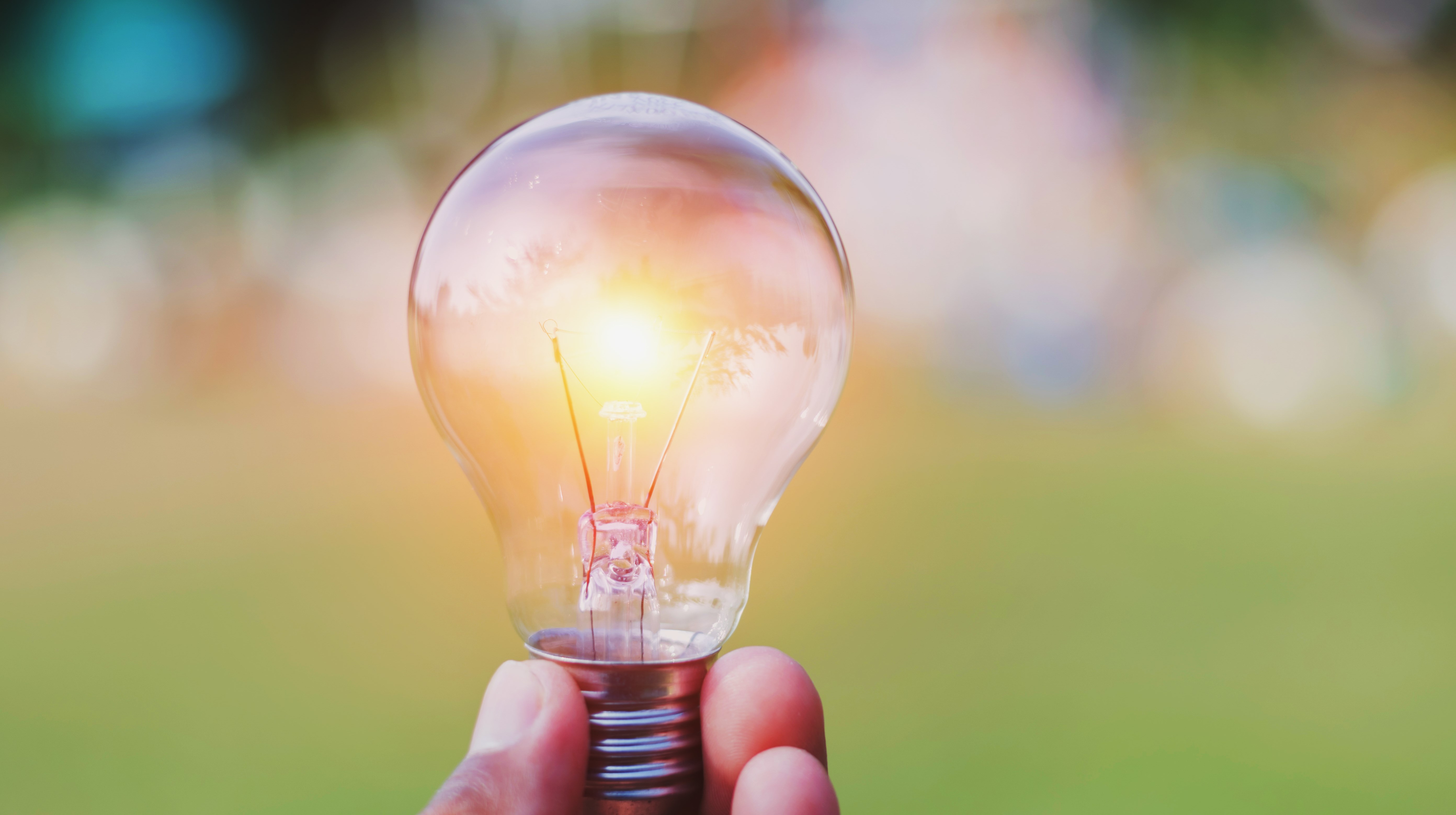 Fingrar som håller i en lysande glödlampa med grön bakgrund