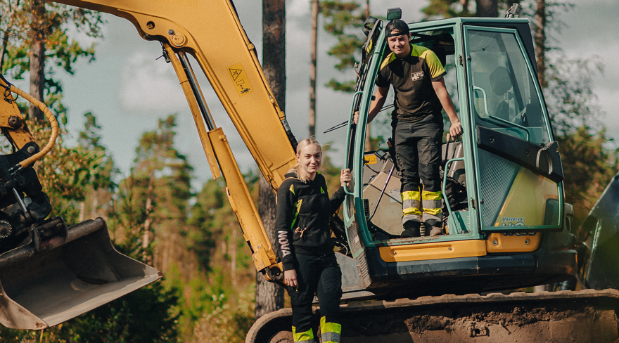 Två elever står vid grävmaskin i skogen