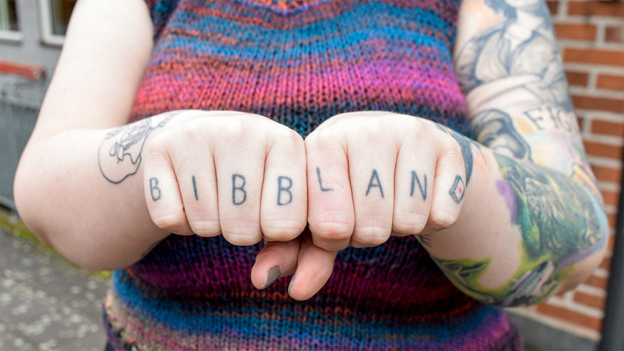 Mikhes knutna händer i fokus. På hennes fingrar är bokstäver tatuerade. Tillsammans bildar de ordet "bibblan".