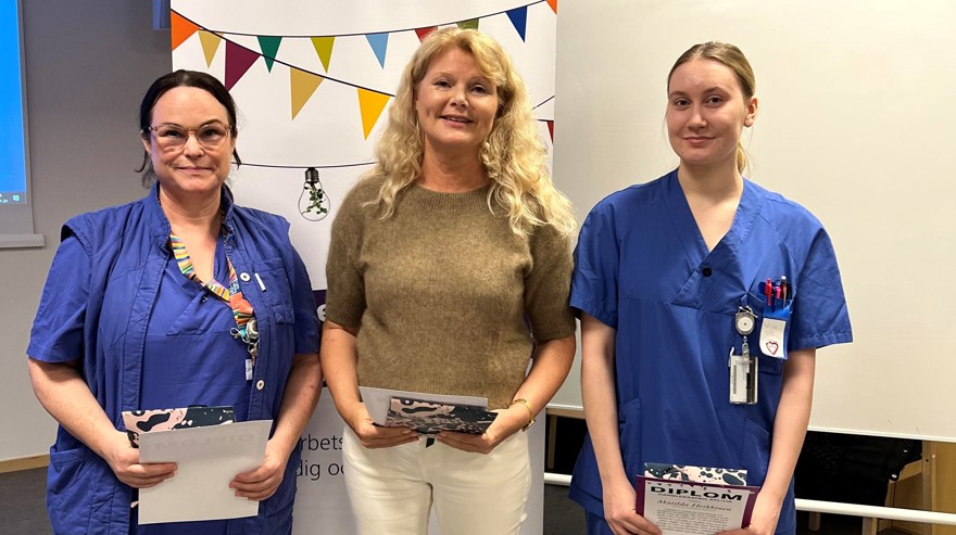 Tre personer ler mot kameran, med diplom i handen.