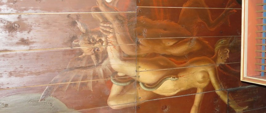 En väggmålning på en trävägg föreställande en djävul som biter en människofigur i benet samtidigt som en orm slingrar sig runt benet på människan.