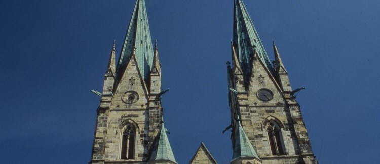 Skara domkyrkas två torn i sten med grönt tak.