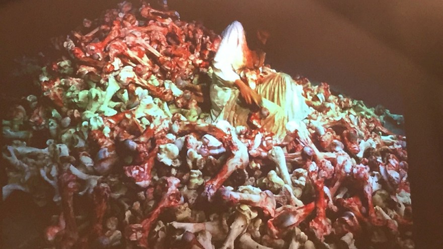 En människa i en vit särk sitter på en hög med blodiga ben.