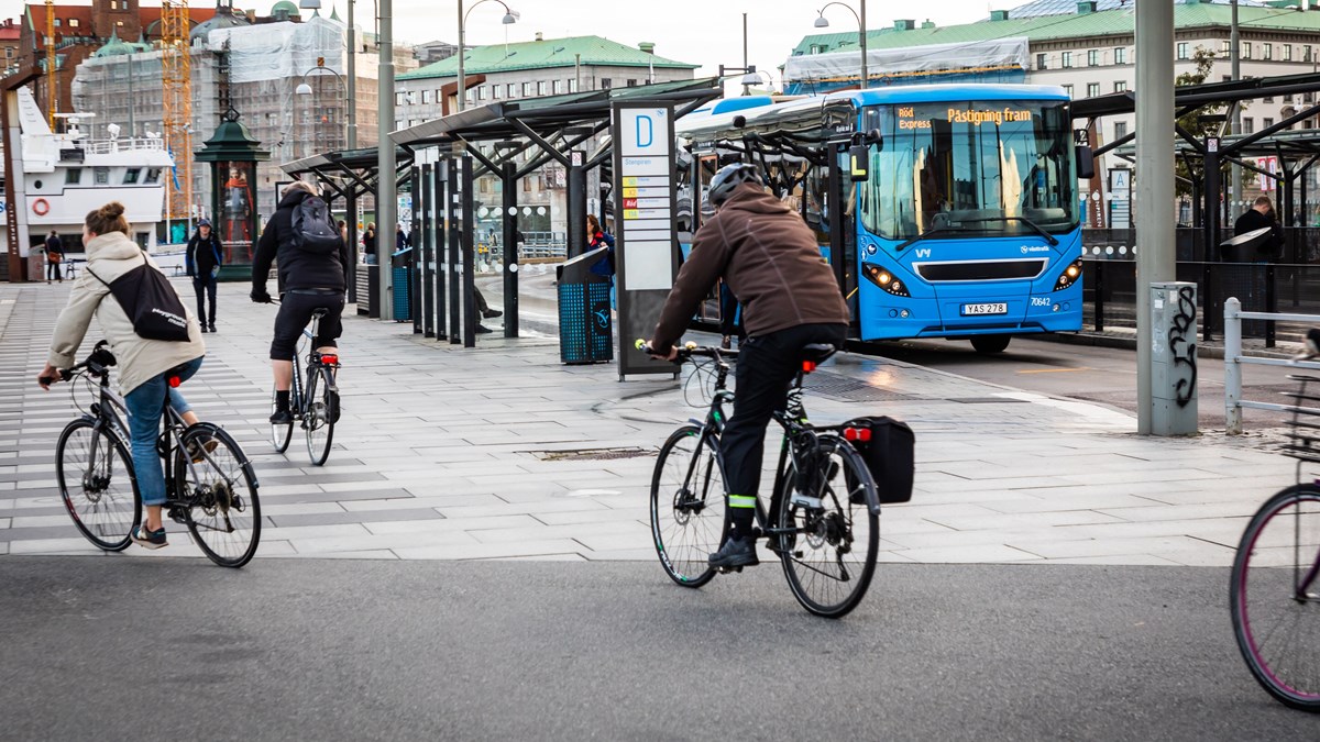 Cyklister passerar på ett torg med en buss vid en hållplats i bakgrunden