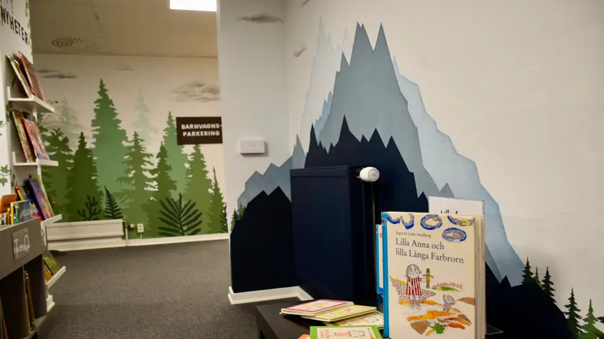 En vägg är målad med spetsiga berg i olika blå kulörer. Framför väggen står ett bord med uppställda böcker.