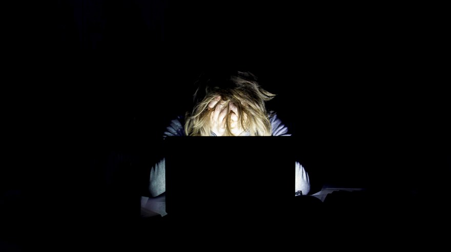 Trött person sitter vid sin laptop i mörkret och river sitt hår.