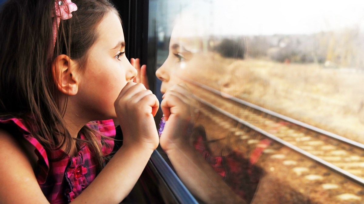 Flicka med hårband med näsan mot tågfönster och tittar ut på landskapet