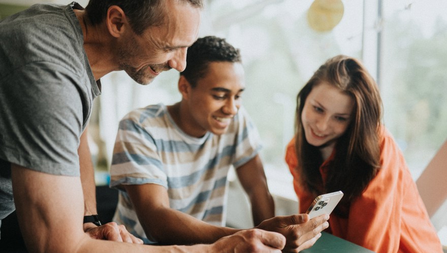 Tre personer tittar i en mobiltelefon