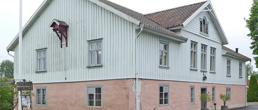 Gäsene tingshus i Herrljunga. En vit träbyggnad med fundament i rosa sten.