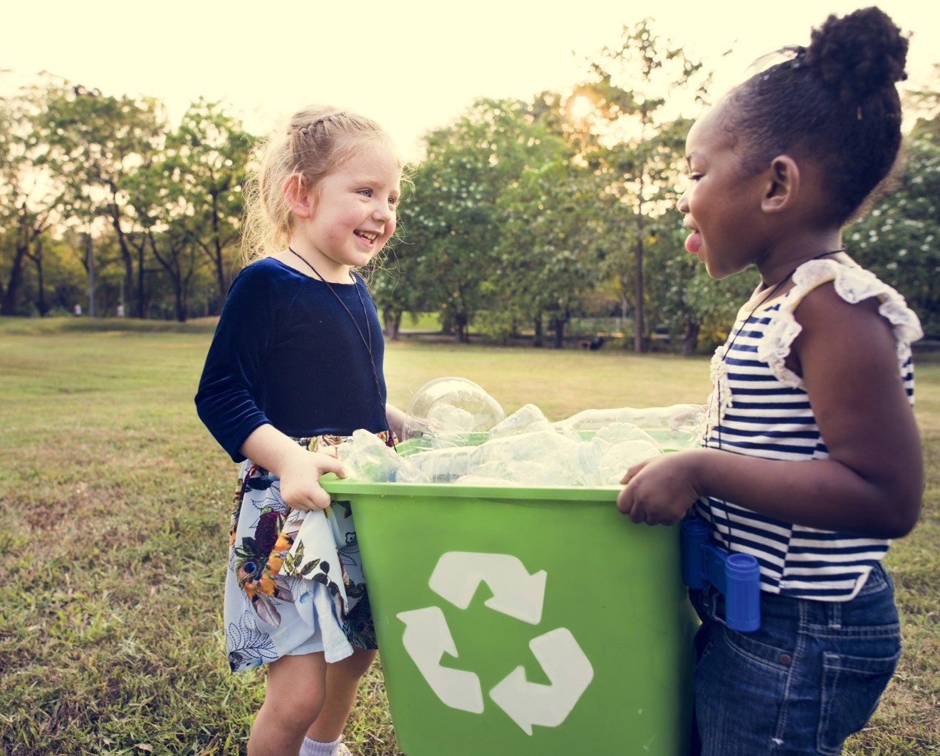 Två barn håller en återvinningstunna mellan sig - stående på en äng