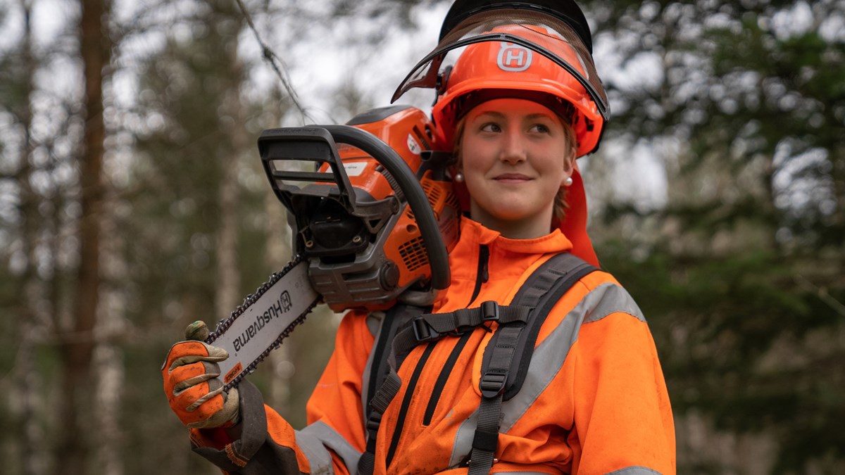  Student wearing protective clothing holds a chainsaw over her shoulder