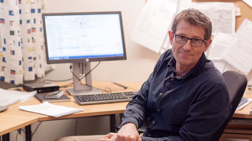 man sitter vid skrivbord och vänder sig mot kameran