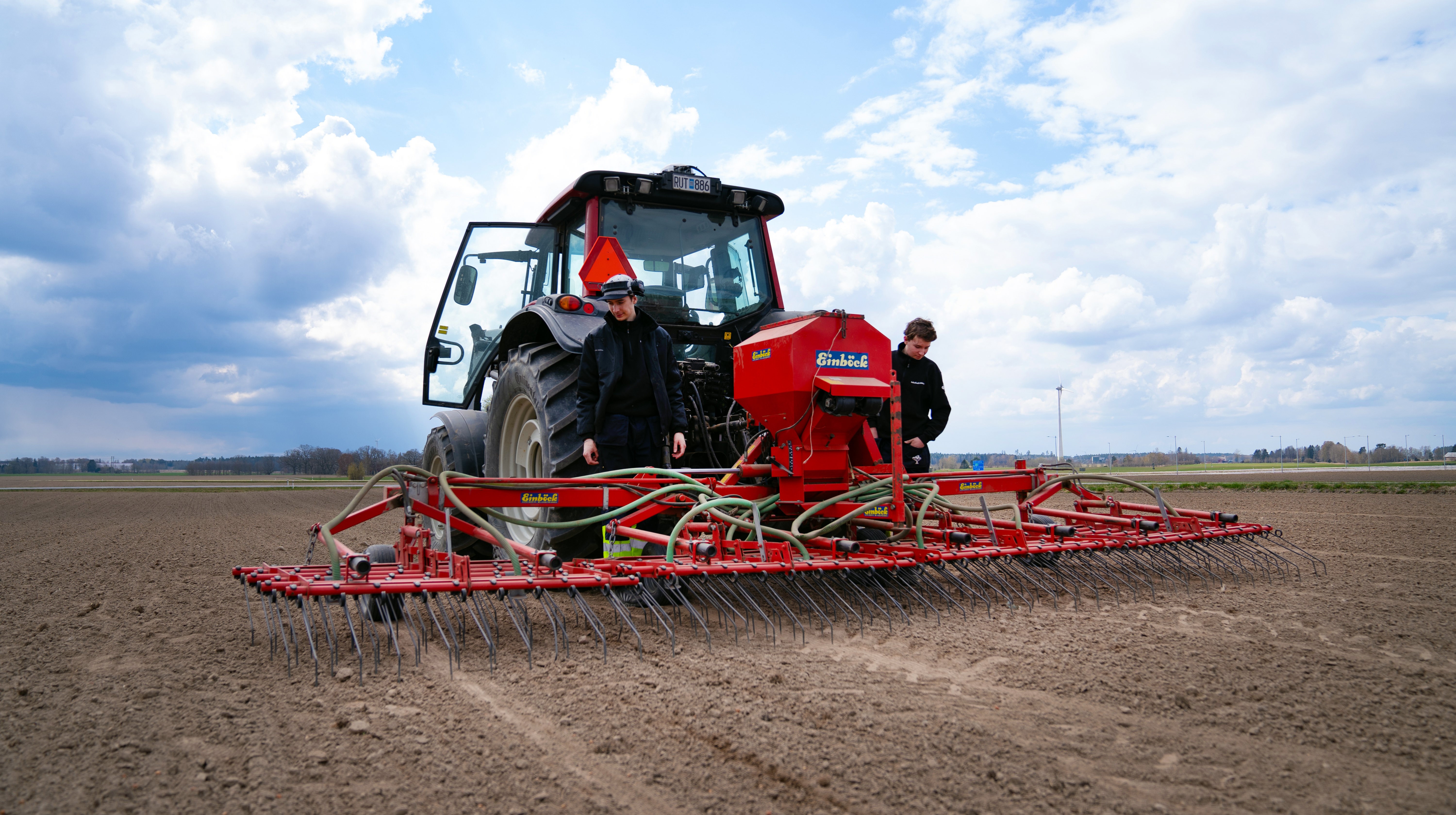 Två elever och en traktor med harv på en åker