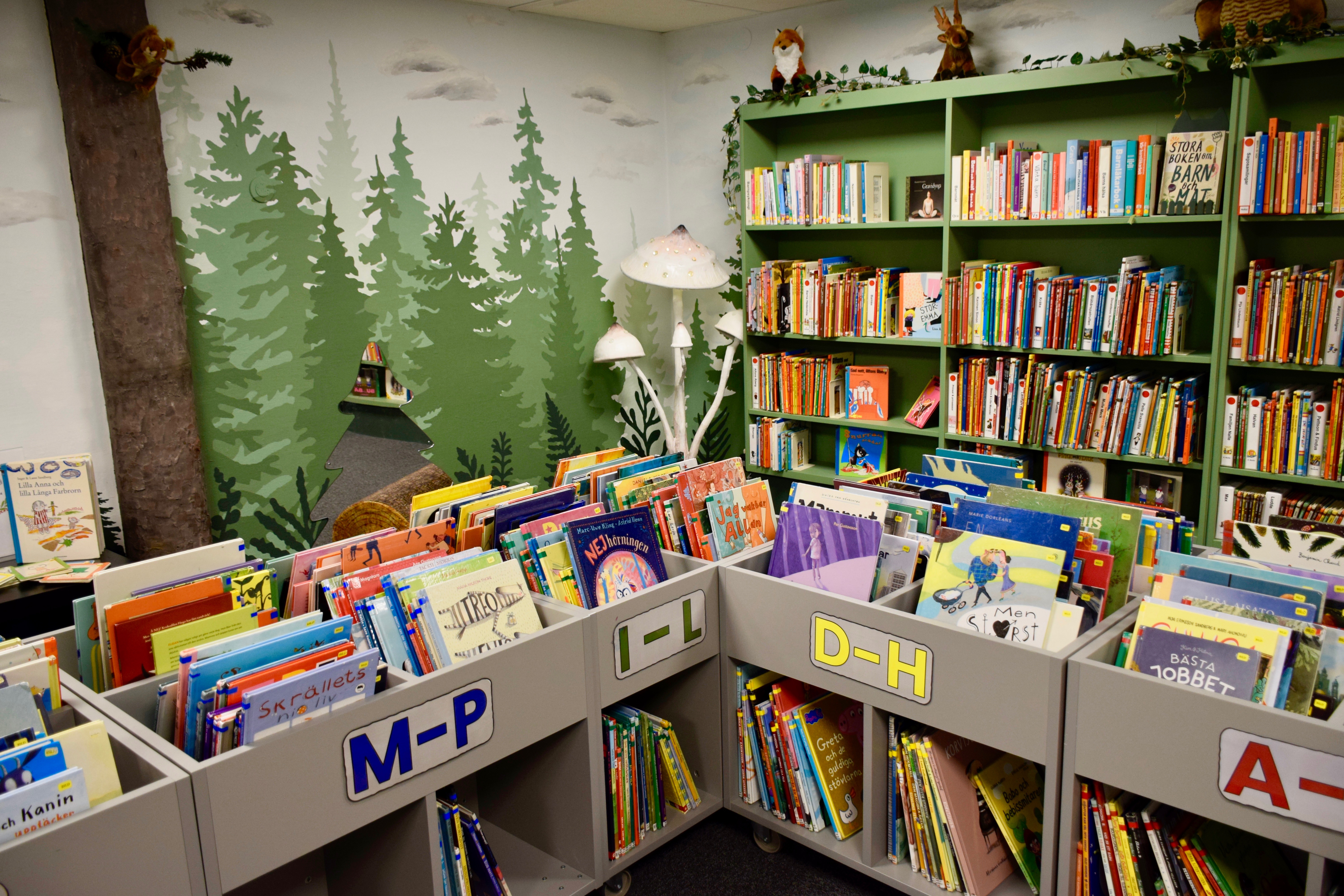 Böcker står i lådor, ordnade i bokstavsordning. I ett hörn står tre vita svampar och överst de höga bokhyllorna finns gosedjur, en räv och en älg. 
