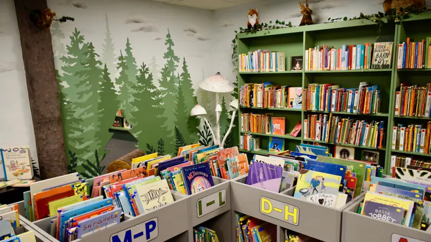 Böcker står i lådor, ordnade i bokstavsordning. I ett hörn står tre vita svampar och överst de höga bokhyllorna finns gosedjur, en räv och en älg.